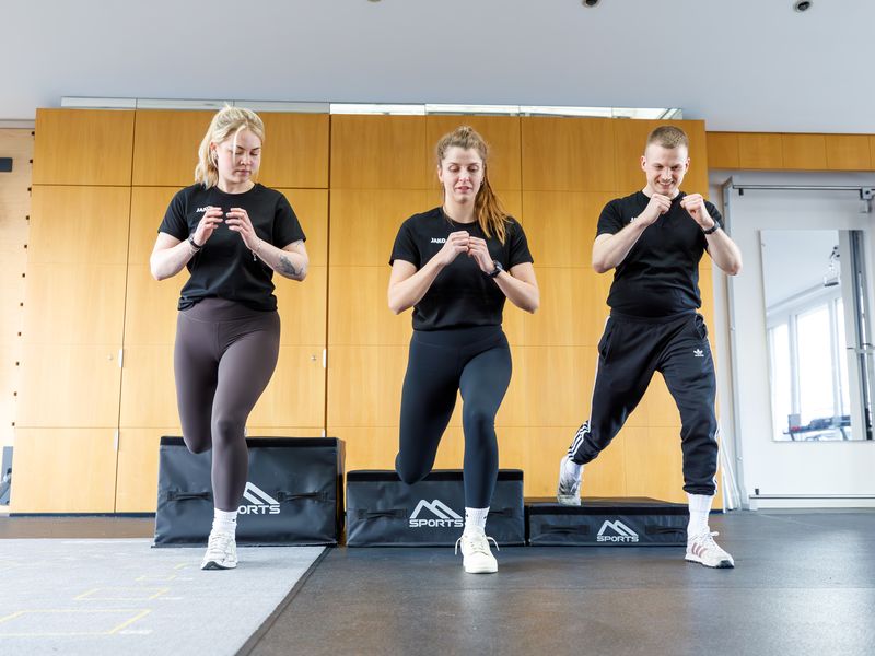 Drei Teammitglieder von myPhysio machen gemeinsam Ausfallschritte in der Trainingsfläche.