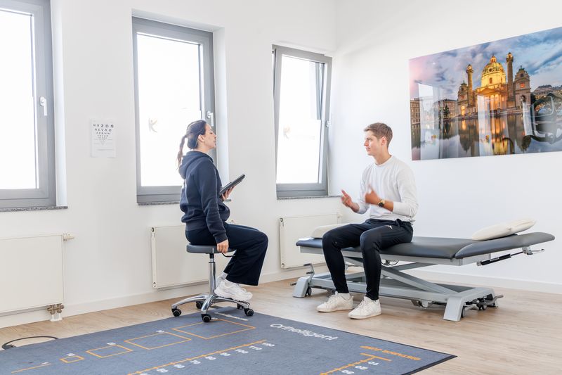 Erstgespräch: Therapeutin mit Tablet und Patient sitzen sich im Behandlungsraum gegenüber.