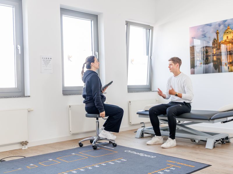 Erstgespräch: Therapeutin mit Tablet und Patient sitzen sich im Behandlungsraum gegenüber.