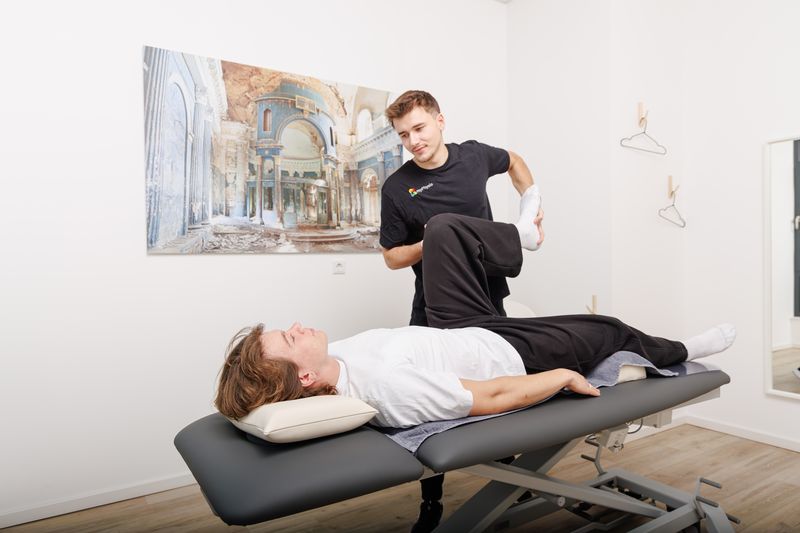 Therapeut hebt das gebeugte Bein eines auf dem Rücken liegenden Patienten an.