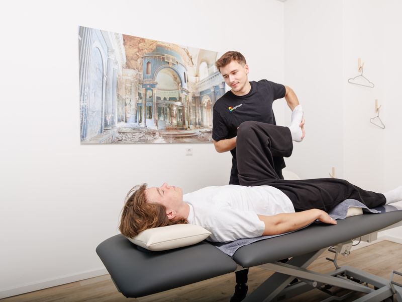 Therapeut hebt das gebeugte Bein eines auf dem Rücken liegenden Patienten an.