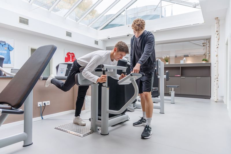 Patient trainiert an einem Beinstreckgerät, der Therapeut steht daneben.
