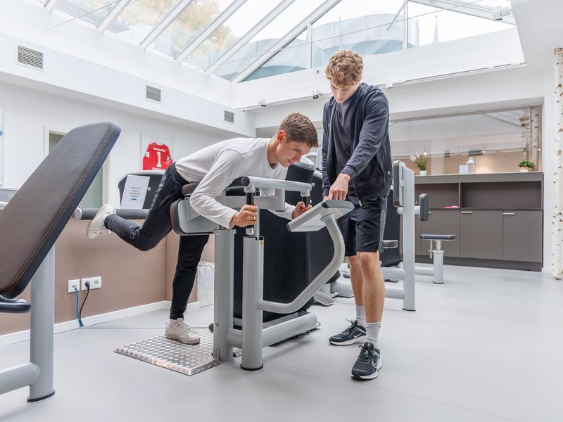 Patient trainiert an einem Beinstreckgerät, der Therapeut steht daneben.