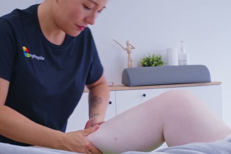 Therapeutin legt beide Hände flach an Knie und Oberschenkel einer liegenden Patientin.