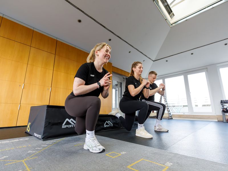 Drei Teammitglieder von myPhysio lachen gemeinsam beim Ausfallschritt.