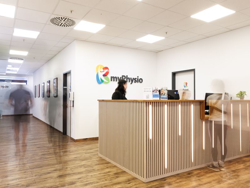 Empfang einer myPhysio-Praxis mit Holzlamellentresen und großem Logo an der Wand.
